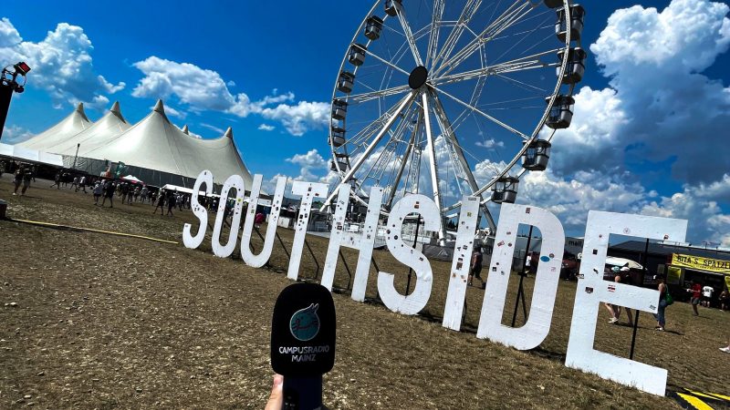 Im Vordergrund ein Aufnahmegerät mit dem Campusradio Mainz Logo, im Hintergrund das Southside Logo auf dem Festivalgelände vor dem Riesenrad.